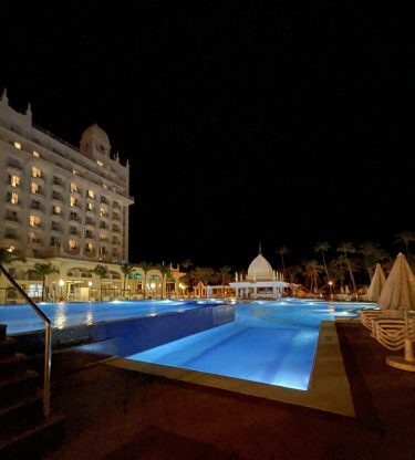 Zicht op het Riu Palace Aruba resort met zwembad en verlichting tijdens de nacht.