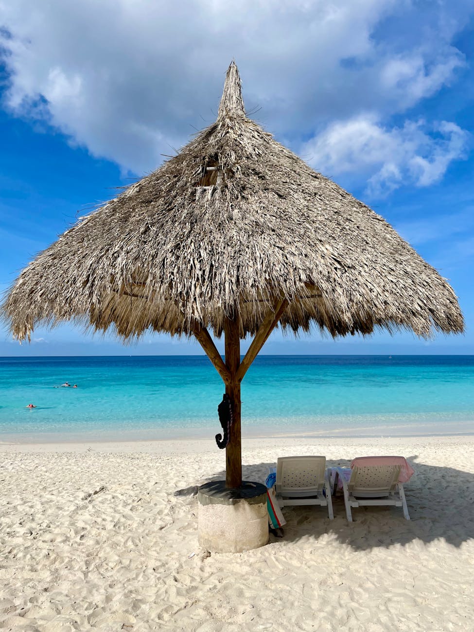 Een strohut op het strand met twee ligstoelen en een uitzicht op het kristalheldere blauwe water van Aruba.